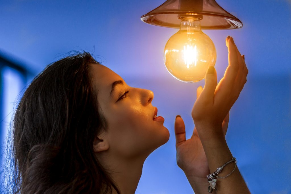 Side profile of a woman gazing at a glowing light bulb, creating a warm and captivating atmosphere.